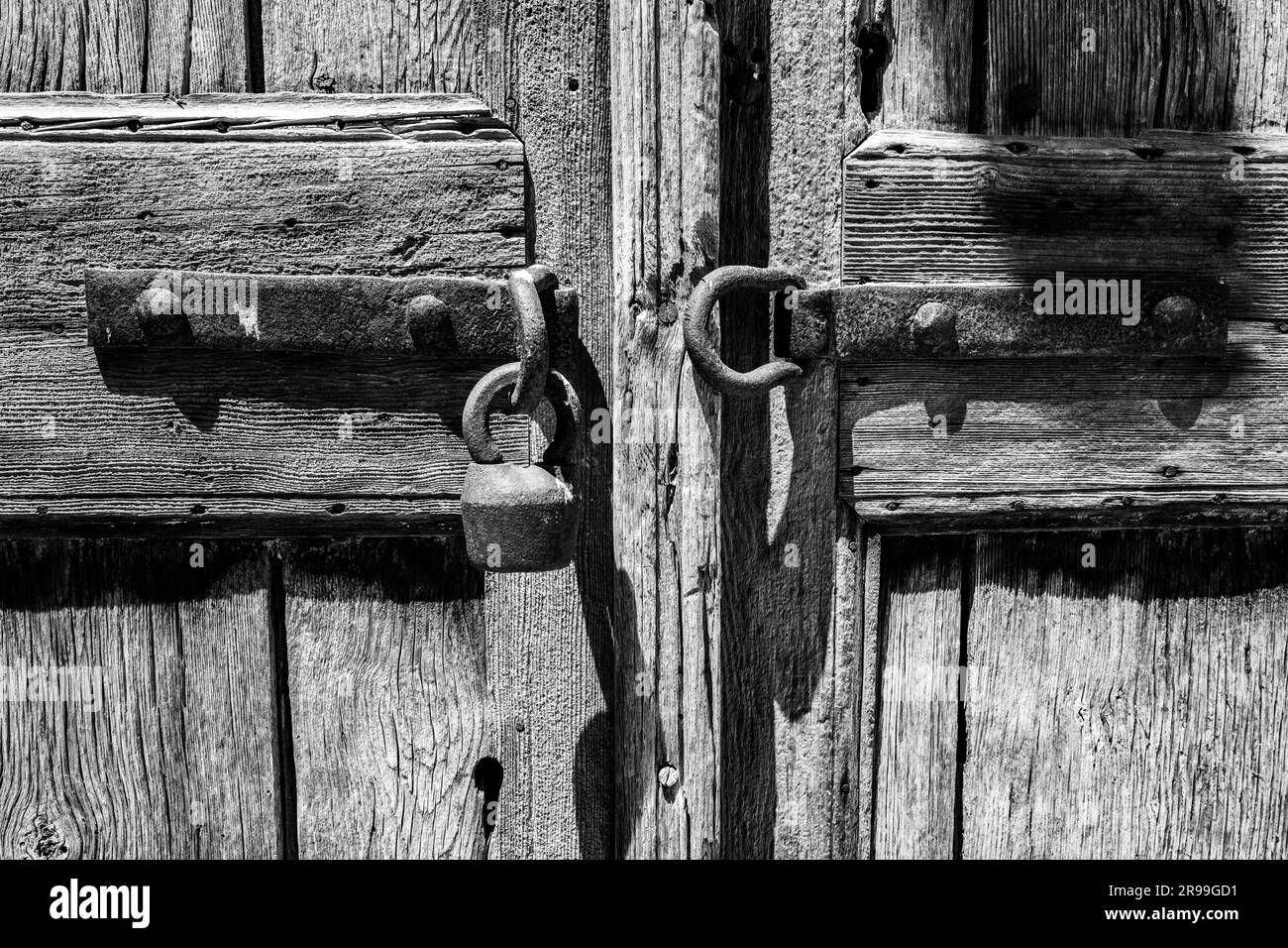 Vue en gros plan d'un cadenas ancien dans une ancienne porte en bois avec motif de grain de bois texturé rugueux. Image noir et blanc. Banque D'Images