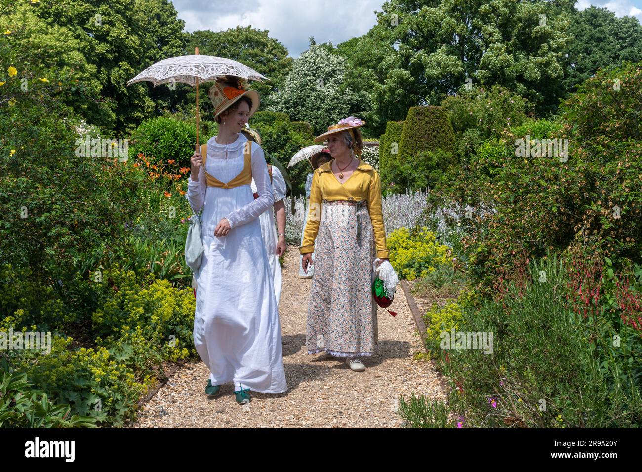 Femmes vêtues de robes victoriennes vintage ou de costumes marchant dans un jardin anglais en été portant des parasols, Angleterre, Royaume-Uni Banque D'Images