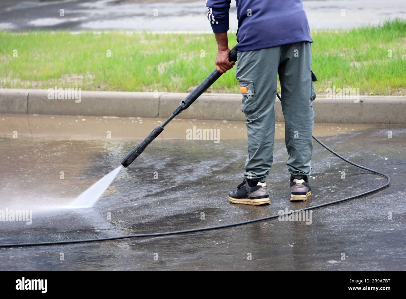 Un travailleur arroser le trottoir avec un tuyau. Nettoyage et désinfection des rues en ville d'été Banque D'Images