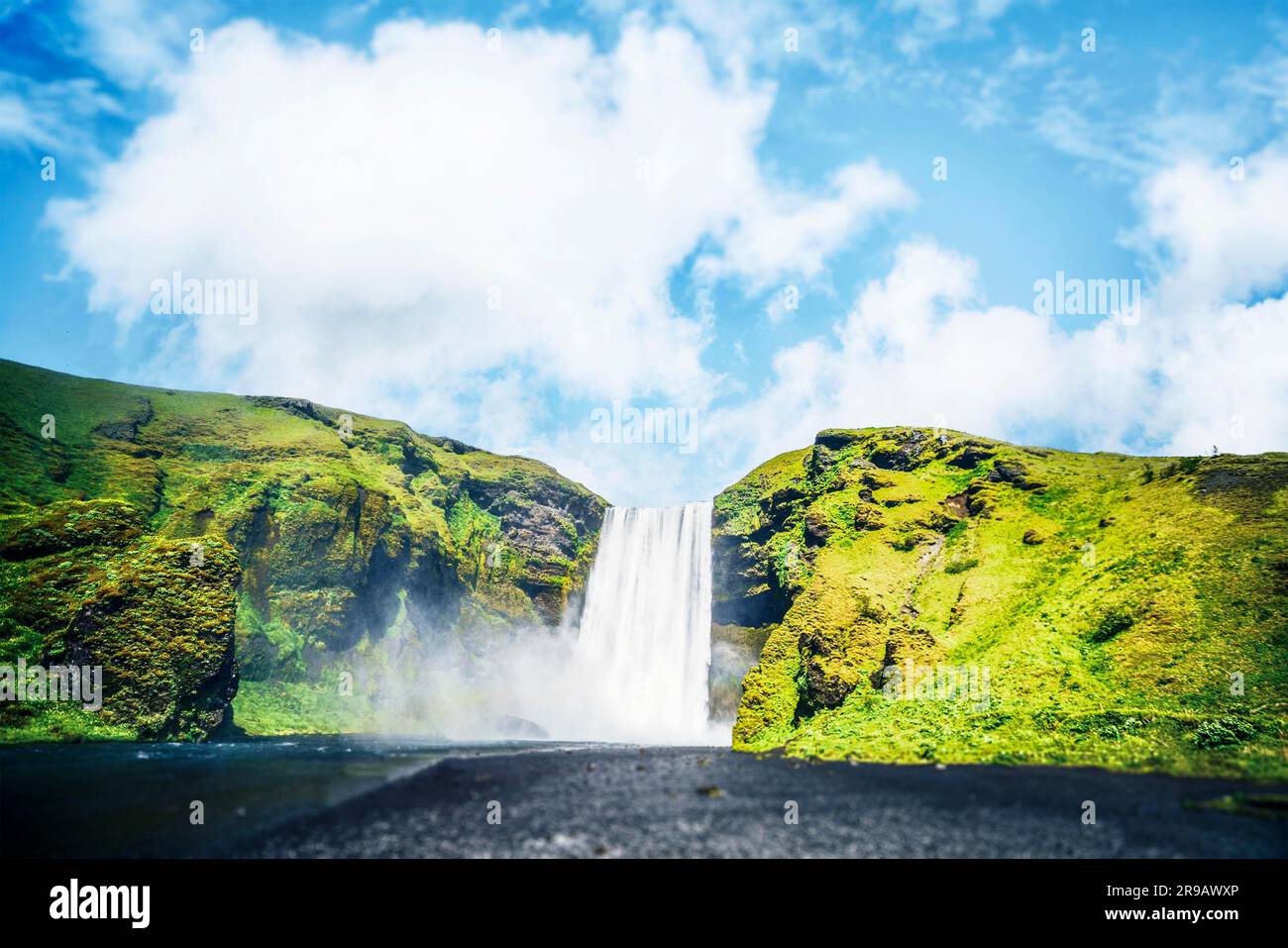 Cascade entre falaises vertes sous un ciel bleu en Islande Banque D'Images