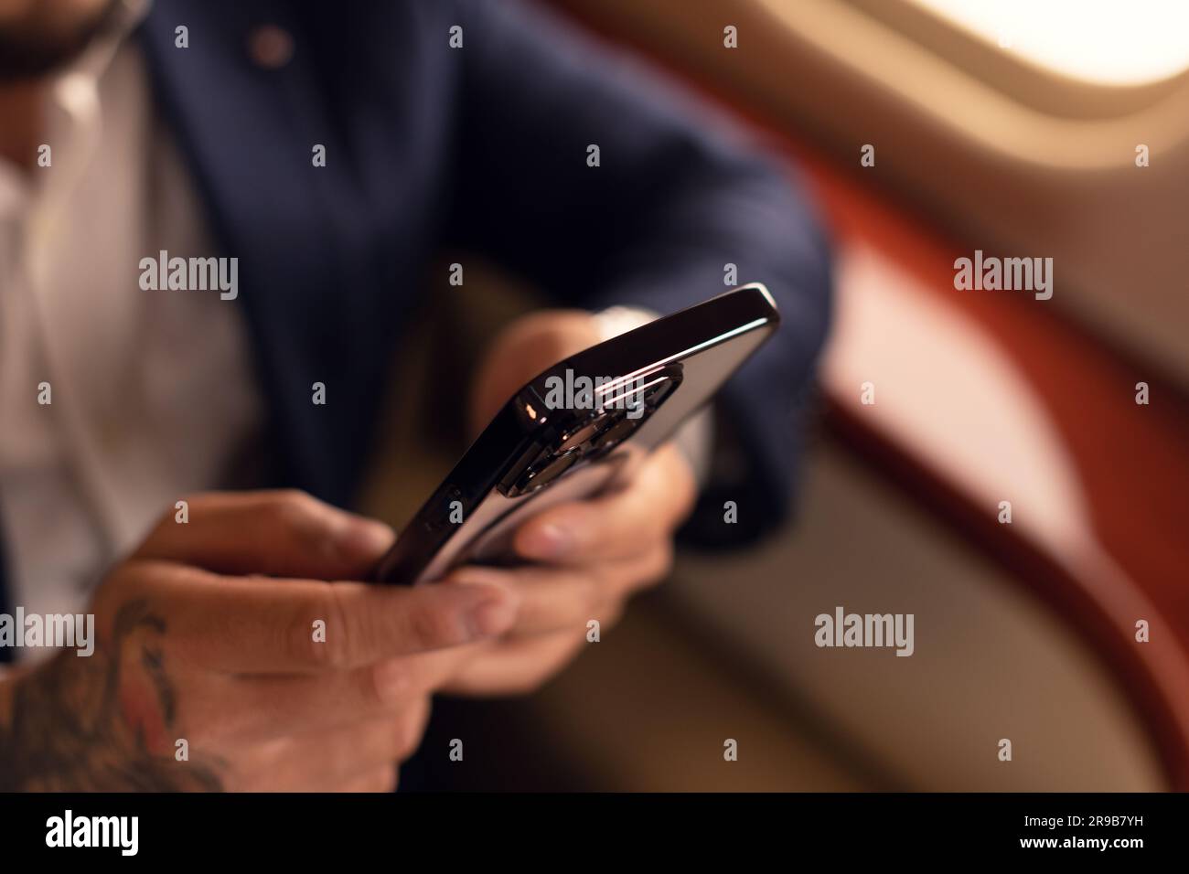 Méconnaissable élégant Jeune homme d'affaires asiatique PDG dans des lunettes et costume homme assis à l'intérieur de la première classe de jet privé tout en travaillant avec smartphone Banque D'Images