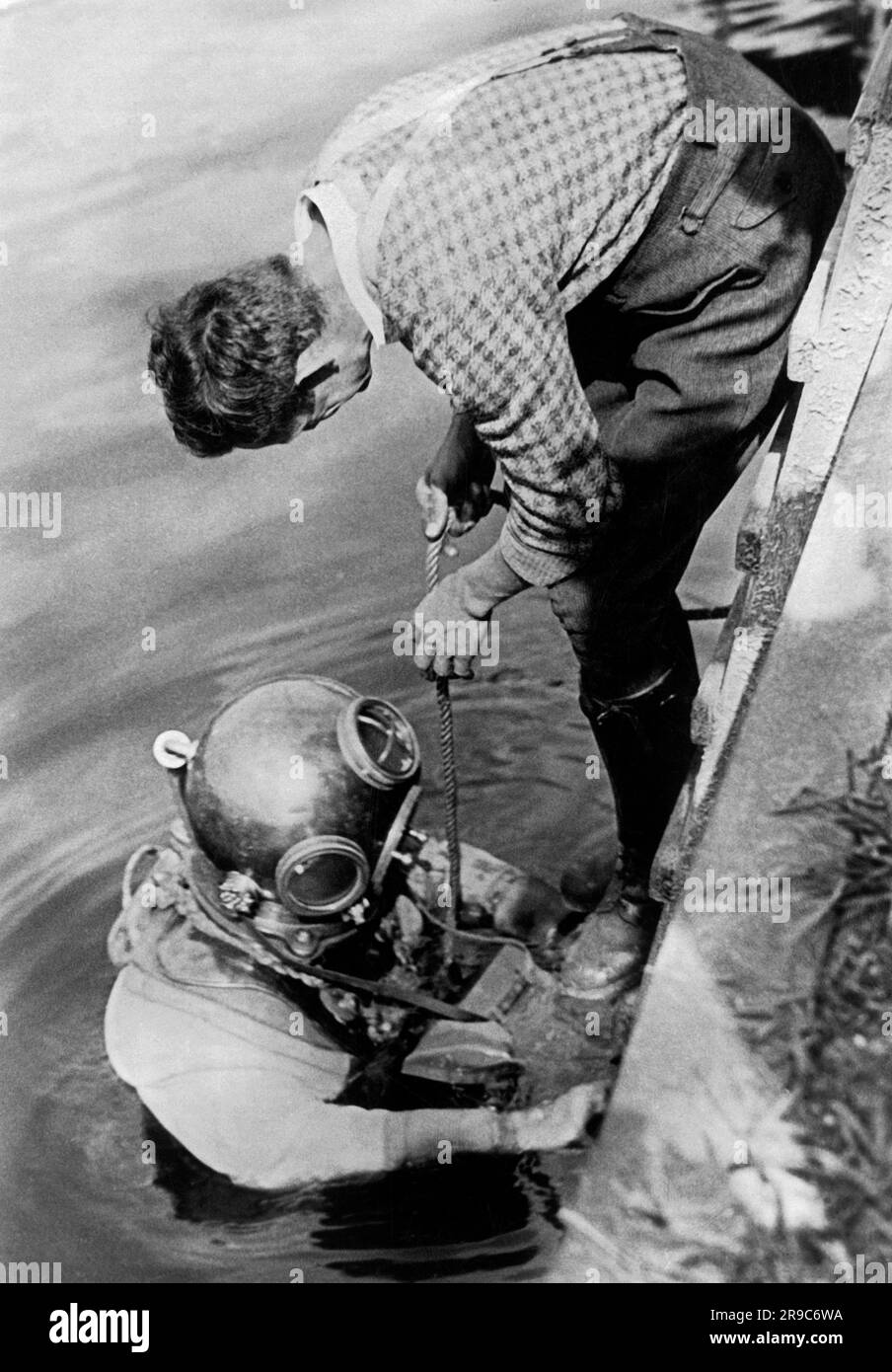 Berlin, Allemagne: c. 1932 le photographe et photojopurnaliste Willie Ruge et son partenaire se préparent à prendre les premières photos sous-marines à l'extérieur d'une cloche de plongée. Leurs chaussures pèsent 36 livres et l'équipement combiné pour cette entreprise sous la surface de la rivière Elbe pesait à 320 livres. Ici, ils reçoivent les instructions finales lorsqu'ils descendent dans la rivière Elbe. Banque D'Images