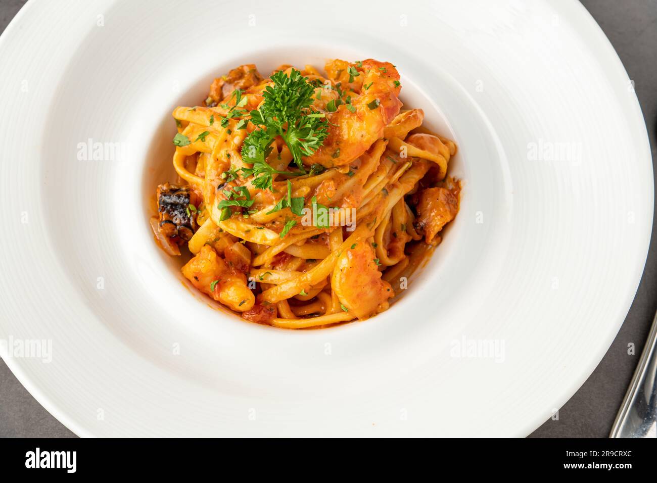 Spaghetti aux crevettes sur une assiette en porcelaine blanche sur une table en pierre noire Banque D'Images