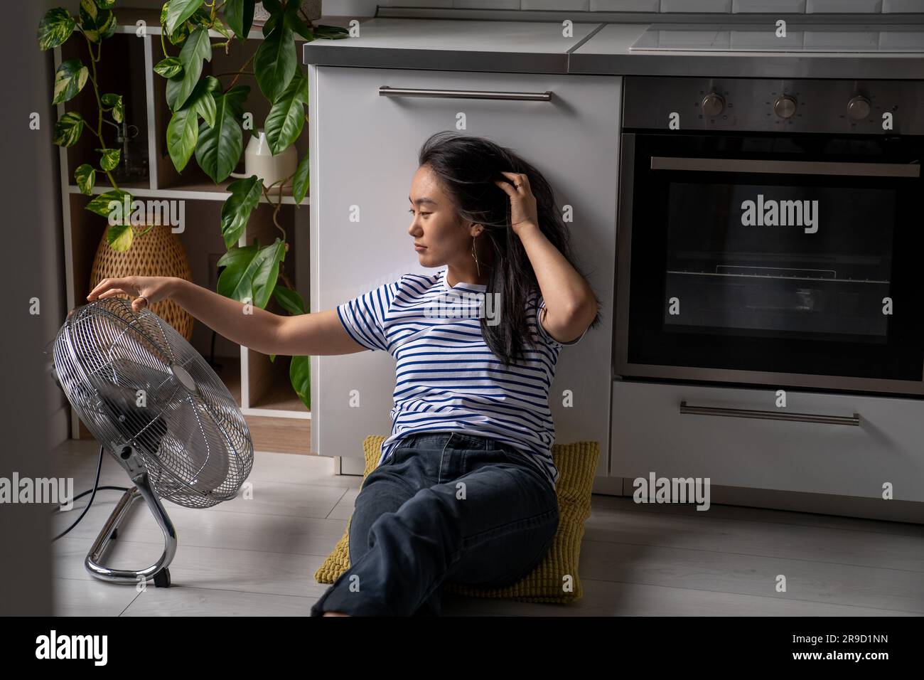 Joyeuse positive asiatique fille aime le vent froid du ventilateur électrique se trouve sur le sol dans la cuisine de la maison Banque D'Images
