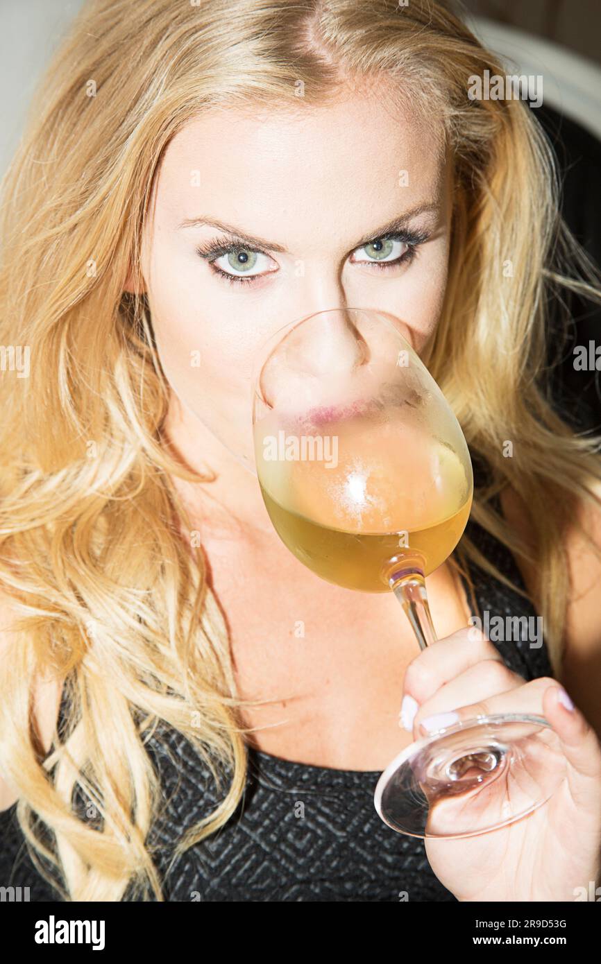 Femme aux yeux verts regardant l'appareil photo sur un grand verre de vin blanc Banque D'Images