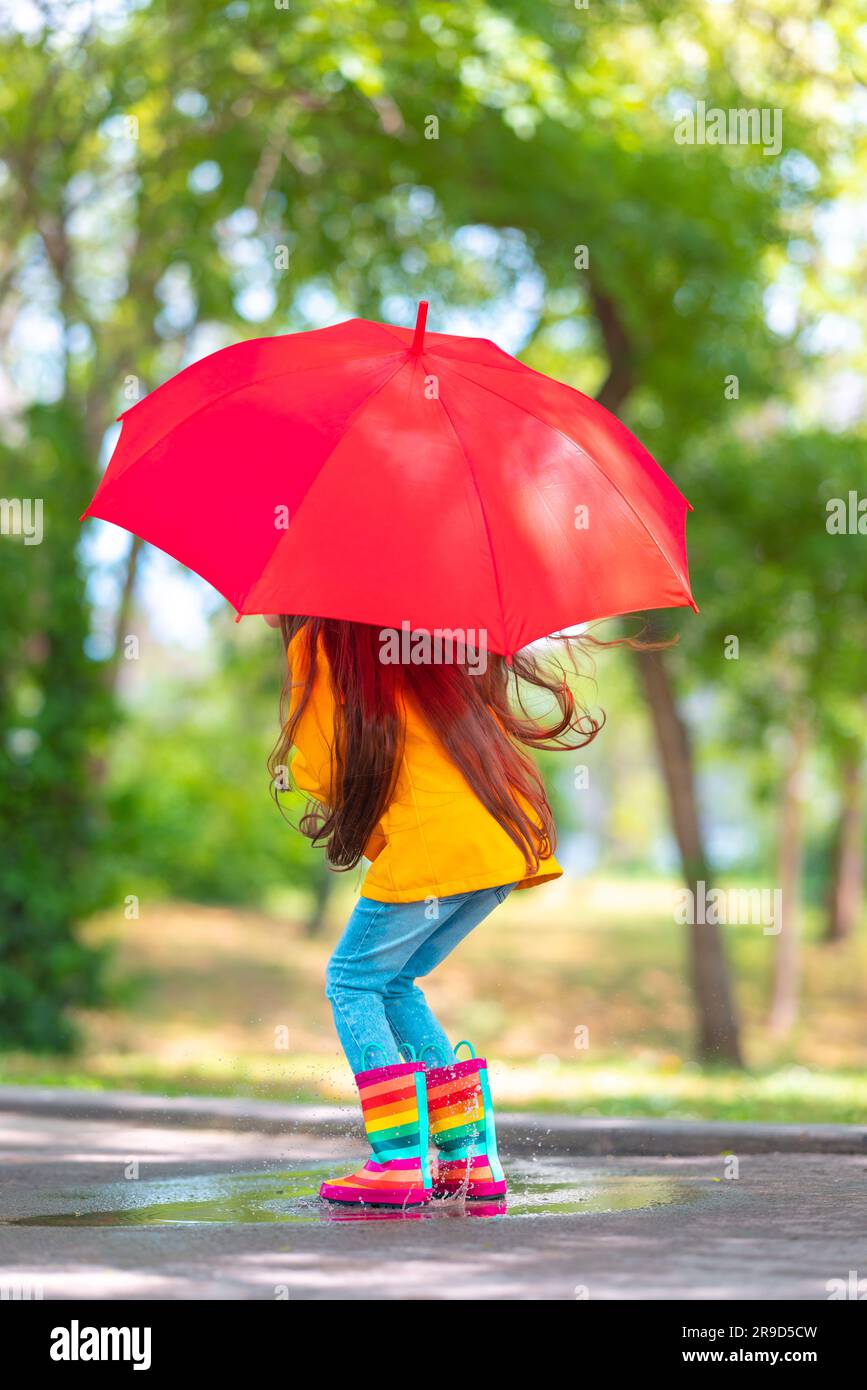 Bonne fille belle avec parapluie et couleur bottes en caoutchouc sauter sur une flaque de pluie Banque D'Images
