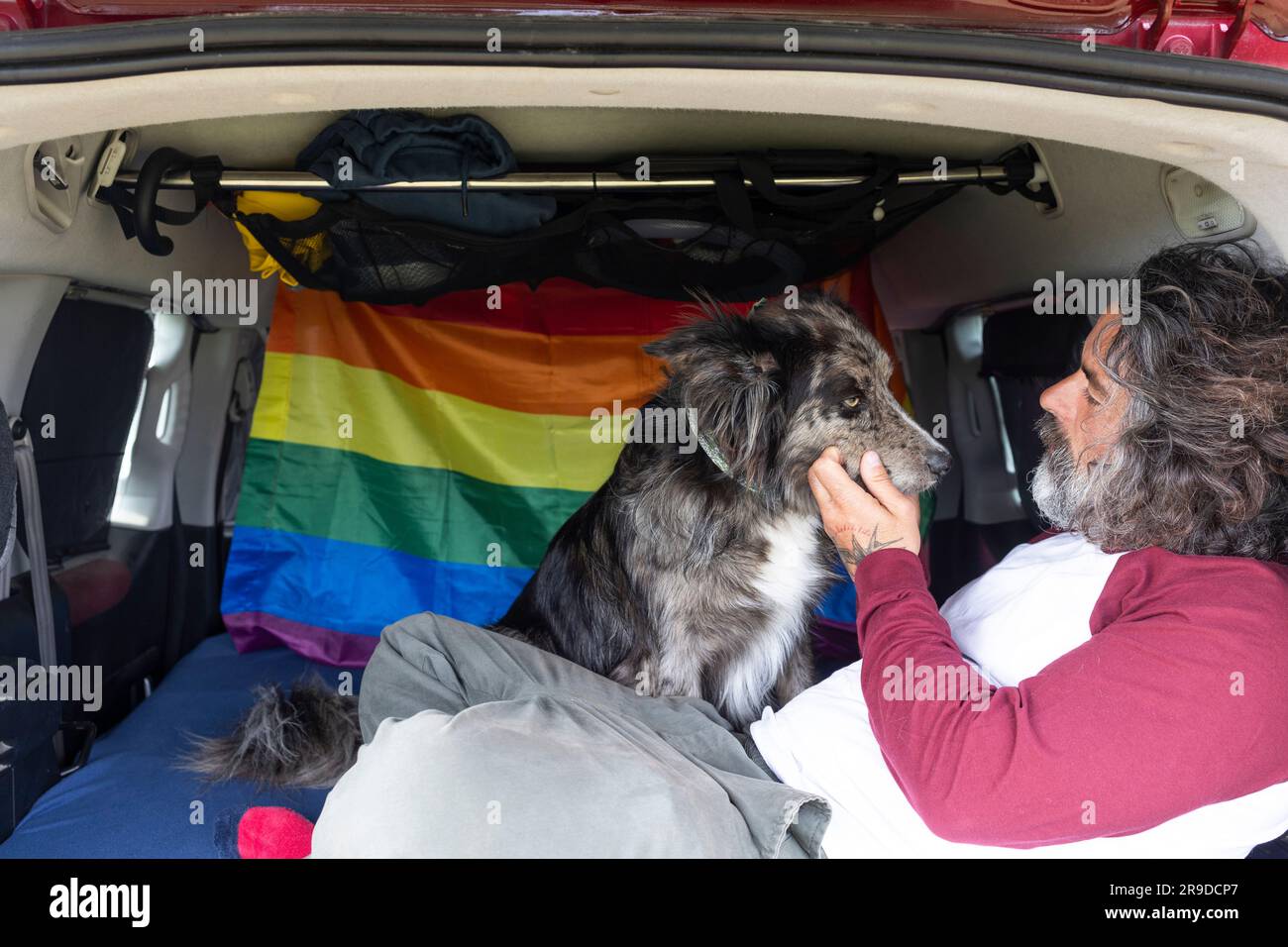 Homme homosexuel assis avec son chien noir sur le lit relaxant et appréciant la journée ensoleillée. Banque D'Images