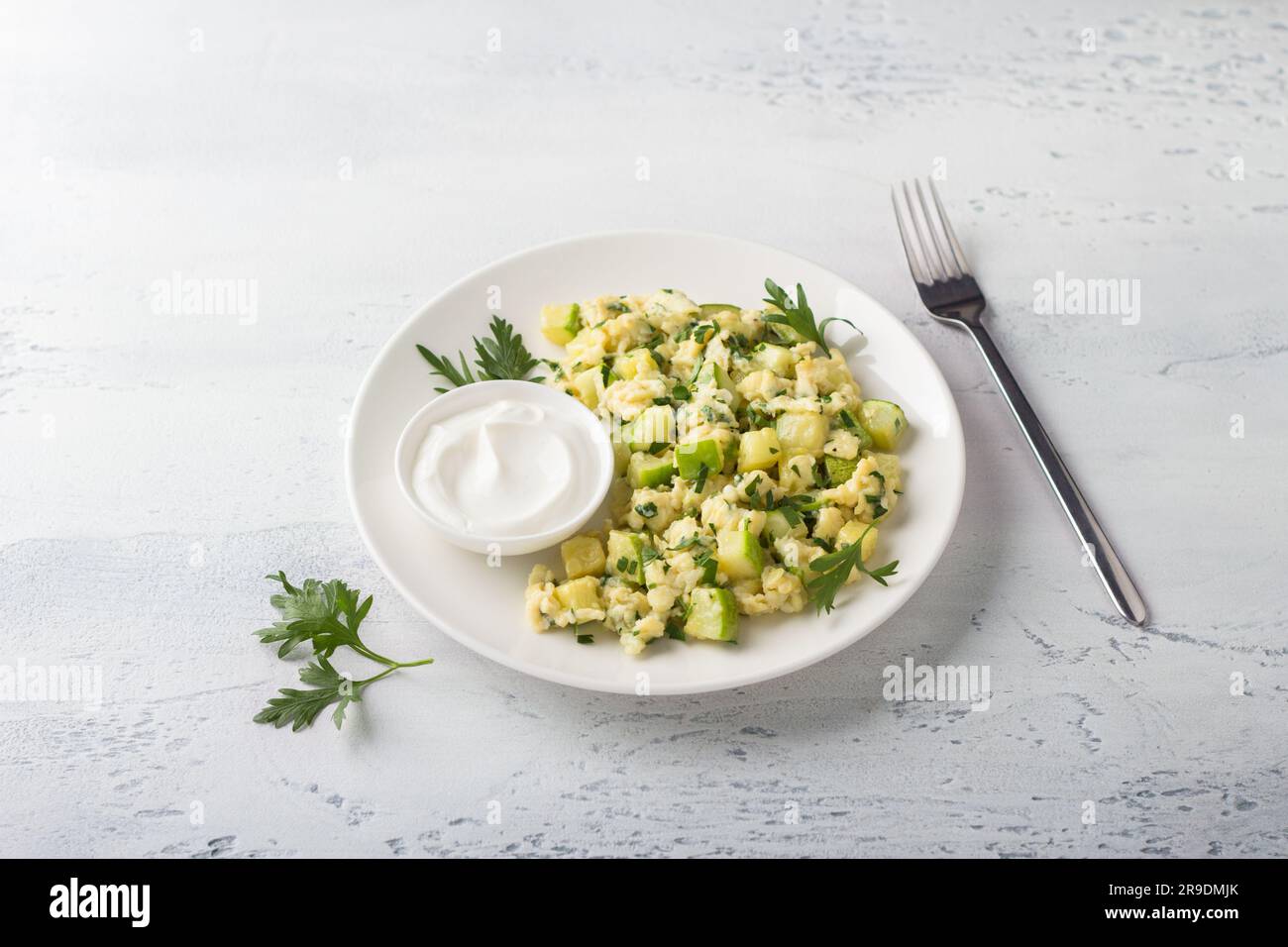 Œufs brouillés turcs avec courgettes servis avec yaourt sur fond bleu clair. Délicieux plats végétariens faits maison. Banque D'Images