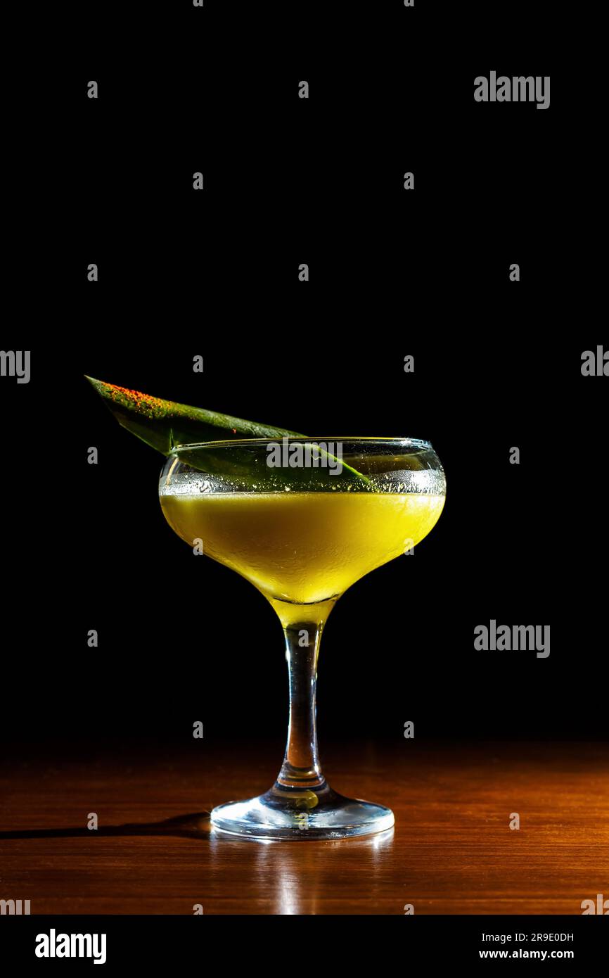 Un cocktail jaune vif est assis dans un verre à l'intérieur - un rafraîchissement alcoolisé parfait pour toute occasion. Banque D'Images