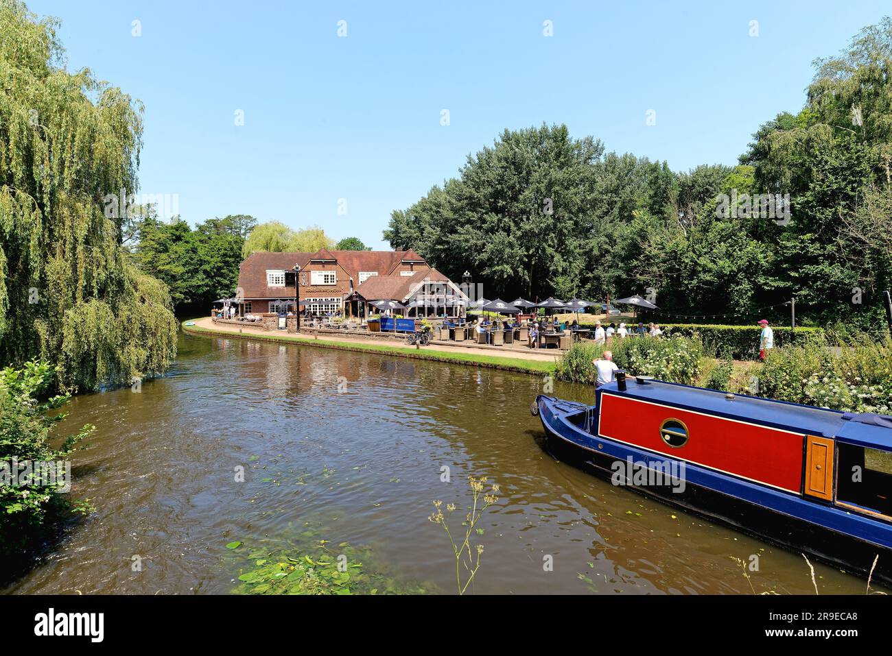 Un bateau étroit passant devant le pub Anchor par Pyrford écluse sur le canal de navigation de River Wey lors d'un chaud jour d'été Surrey Angleterre Royaume-Uni Banque D'Images