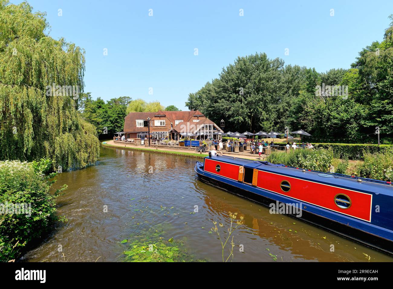 Un bateau étroit passant devant le pub Anchor par Pyrford écluse sur le canal de navigation de River Wey lors d'un chaud jour d'été Surrey Angleterre Royaume-Uni Banque D'Images