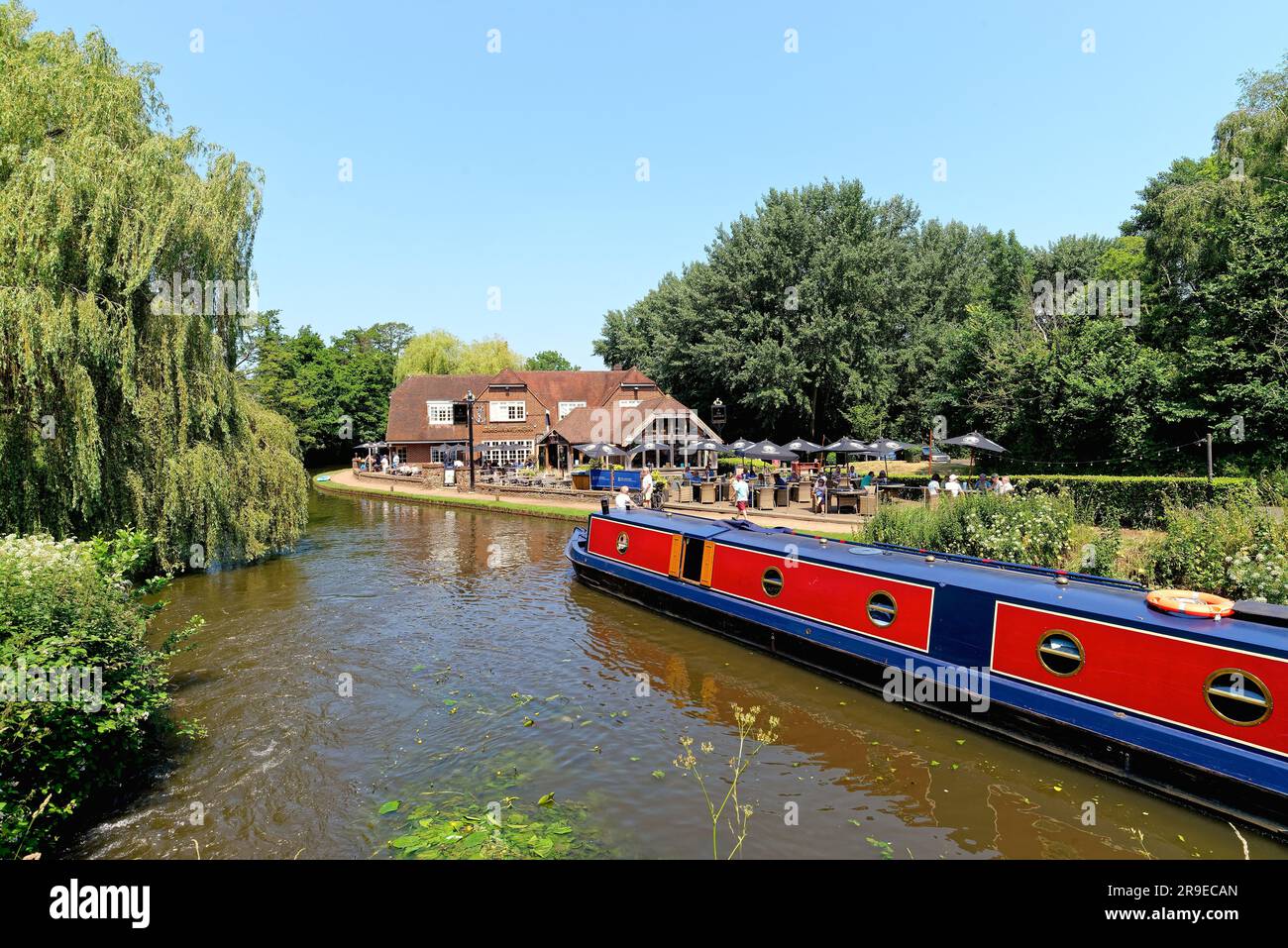 Un bateau étroit passant devant le pub Anchor par Pyrford écluse sur le canal de navigation de River Wey lors d'un chaud jour d'été Surrey Angleterre Royaume-Uni Banque D'Images