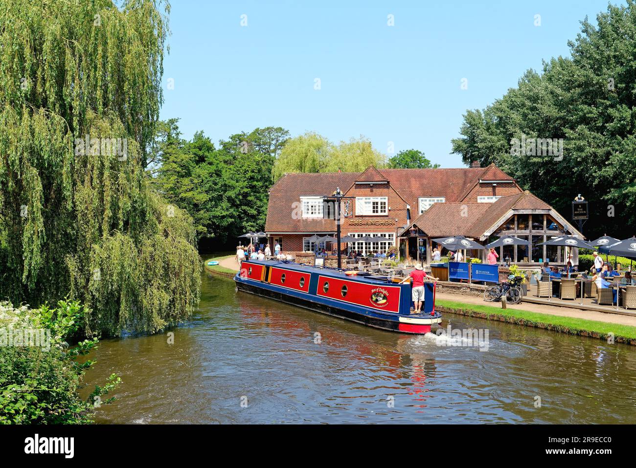 Un bateau étroit passant devant le pub Anchor par Pyrford écluse sur le canal de navigation de River Wey lors d'un chaud jour d'été Surrey Angleterre Royaume-Uni Banque D'Images