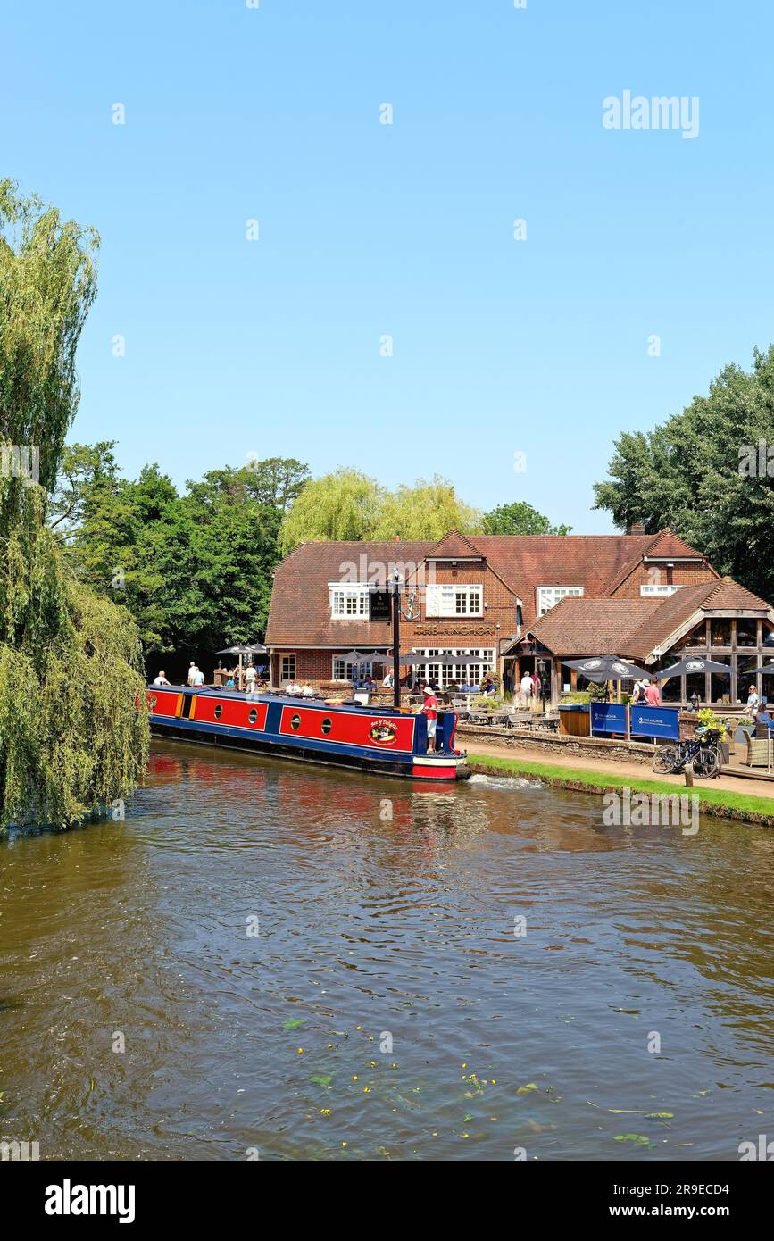Un bateau étroit passant devant le pub Anchor par Pyrford écluse sur le canal de navigation de River Wey lors d'un chaud jour d'été Surrey Angleterre Royaume-Uni Banque D'Images