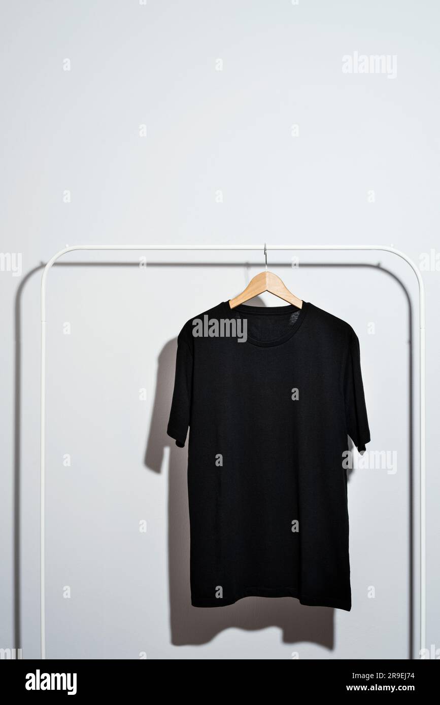 Maquette de t-shirt noir vierge, modèle sur cintre en bois sur un porte-vêtements blanc Banque D'Images