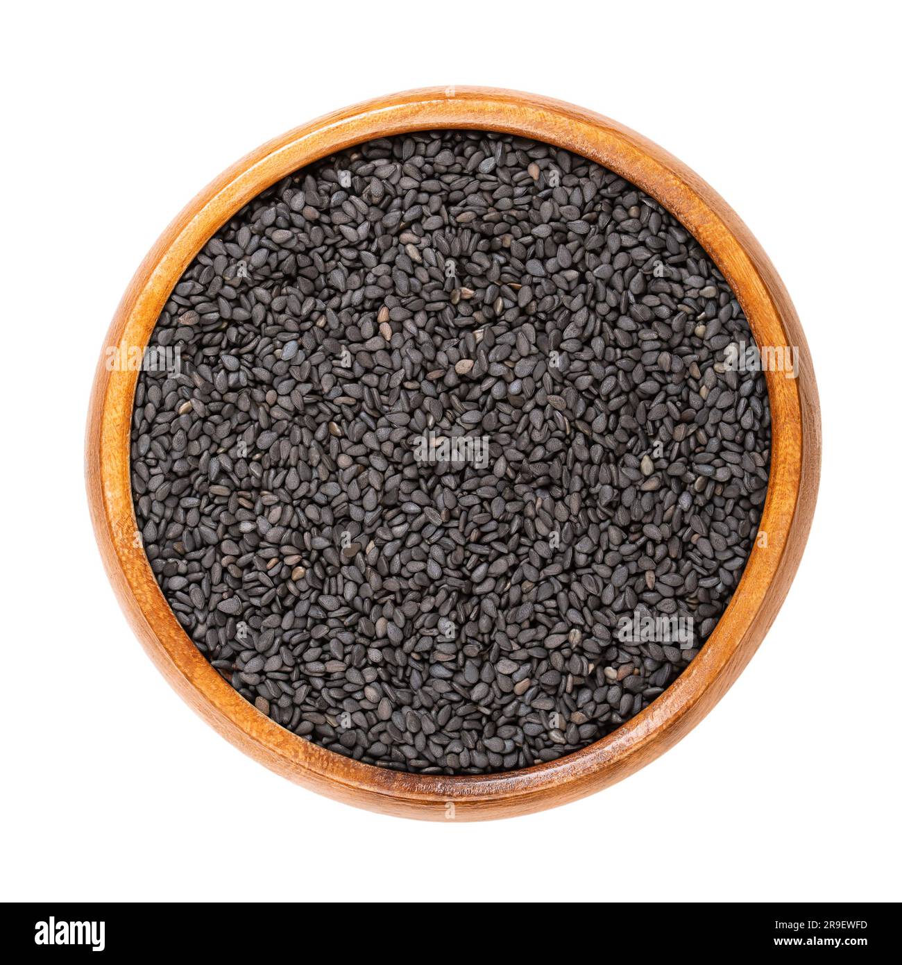 Sésame noir, dans un bol en bois. Graines non décortiquées de Sesamum indicum, riches et de saveur noisette, avec une des plus fortes teneur en huile de toute graine. Banque D'Images