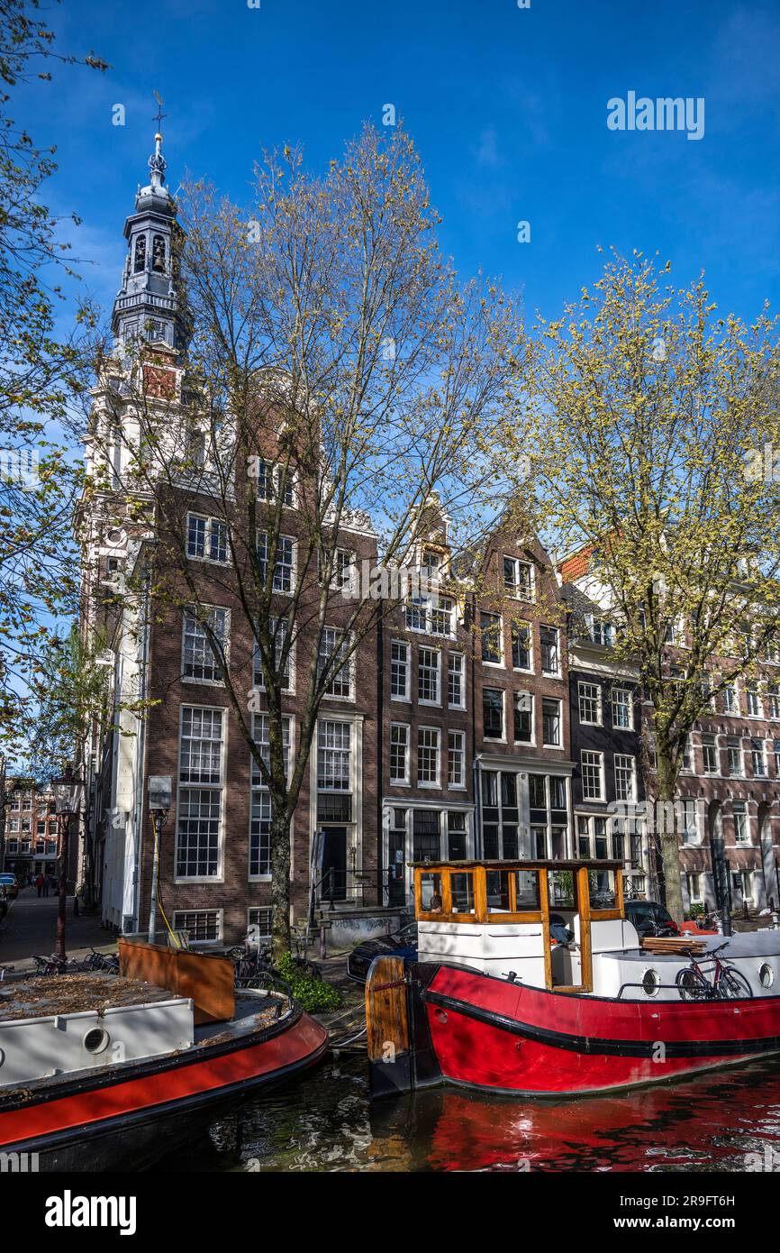 péniche aménagée sur un canal à Amsterdam avec la tour de l'église de Kuiderkerk au loin et maisons de canal Banque D'Images