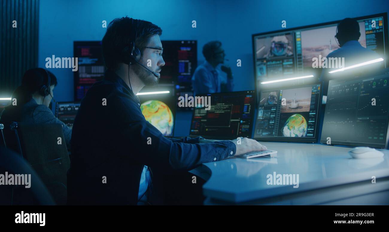 L'opérateur de contrôle de vol dans le casque se trouve devant les ordinateurs du centre de contrôle de mission, surveille la mission spatiale. Un groupe de travailleurs claque les mains après le décollage de l'engin spatial sur de grands écrans numériques. Banque D'Images