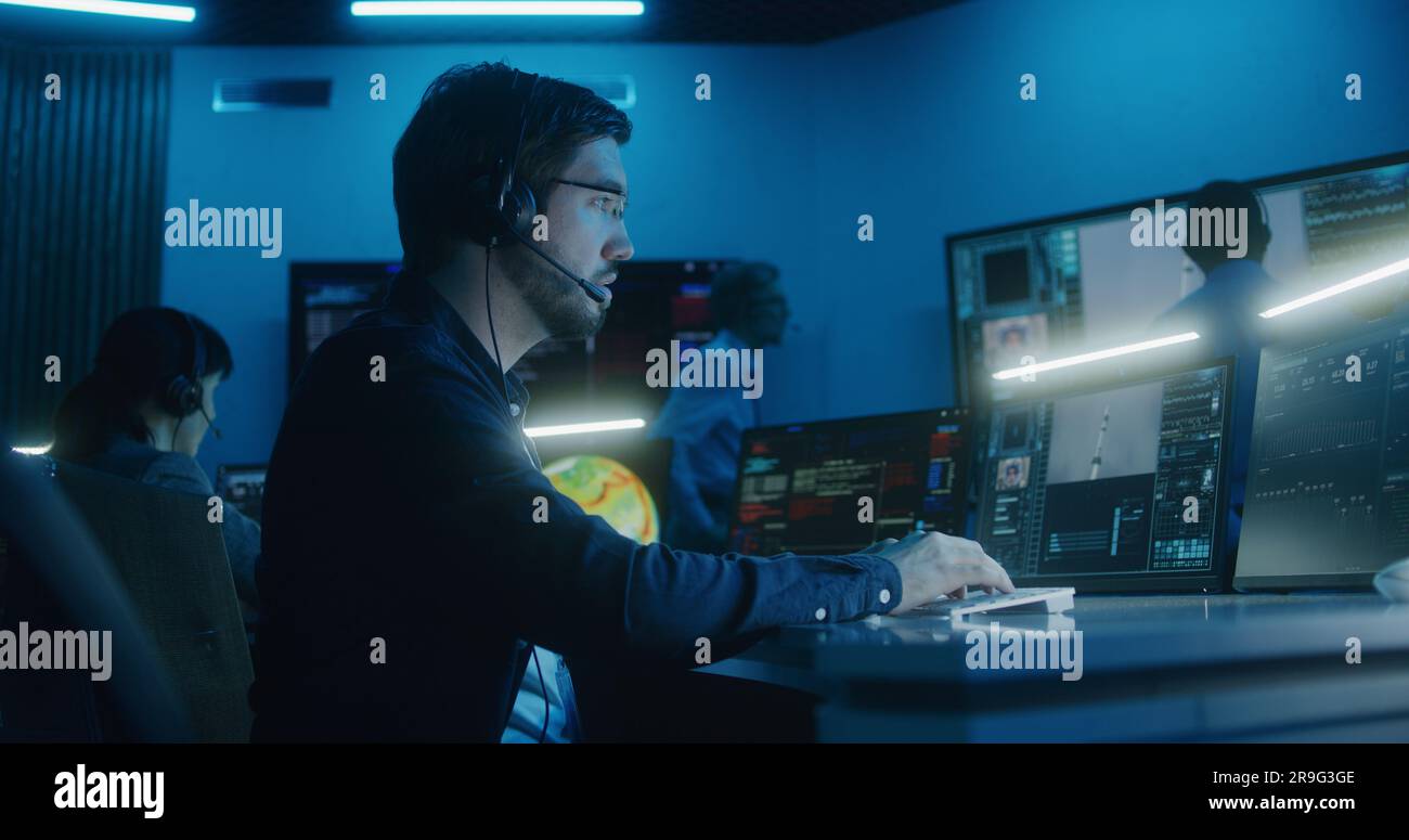 L'opérateur de contrôle de vol dans le casque se trouve devant les ordinateurs du centre de contrôle de mission, surveille la mission spatiale. Un groupe de travailleurs claque les mains après le décollage de l'engin spatial sur de grands écrans numériques. Banque D'Images