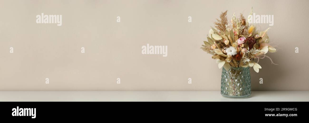 Beau bouquet de fleurs séchées dans vase en verre sur table près du mur beige, espace pour le texte. Bannière Banque D'Images