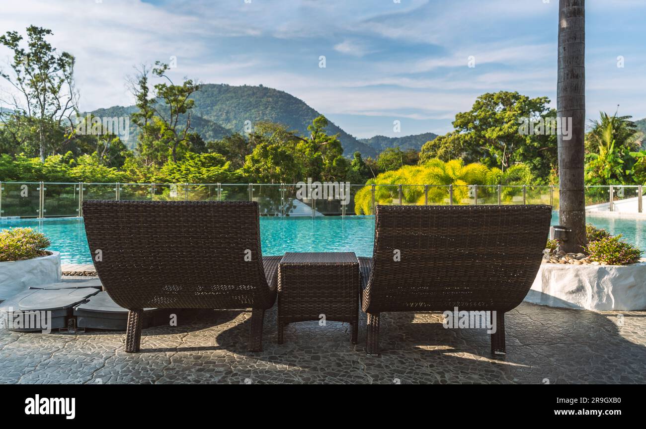 Deux chaises longues en osier et un bureau à la piscine de luxe avec le fond de paysage de montagne et le ciel bleu, vue de derrière deux bains de soleil en osier Banque D'Images