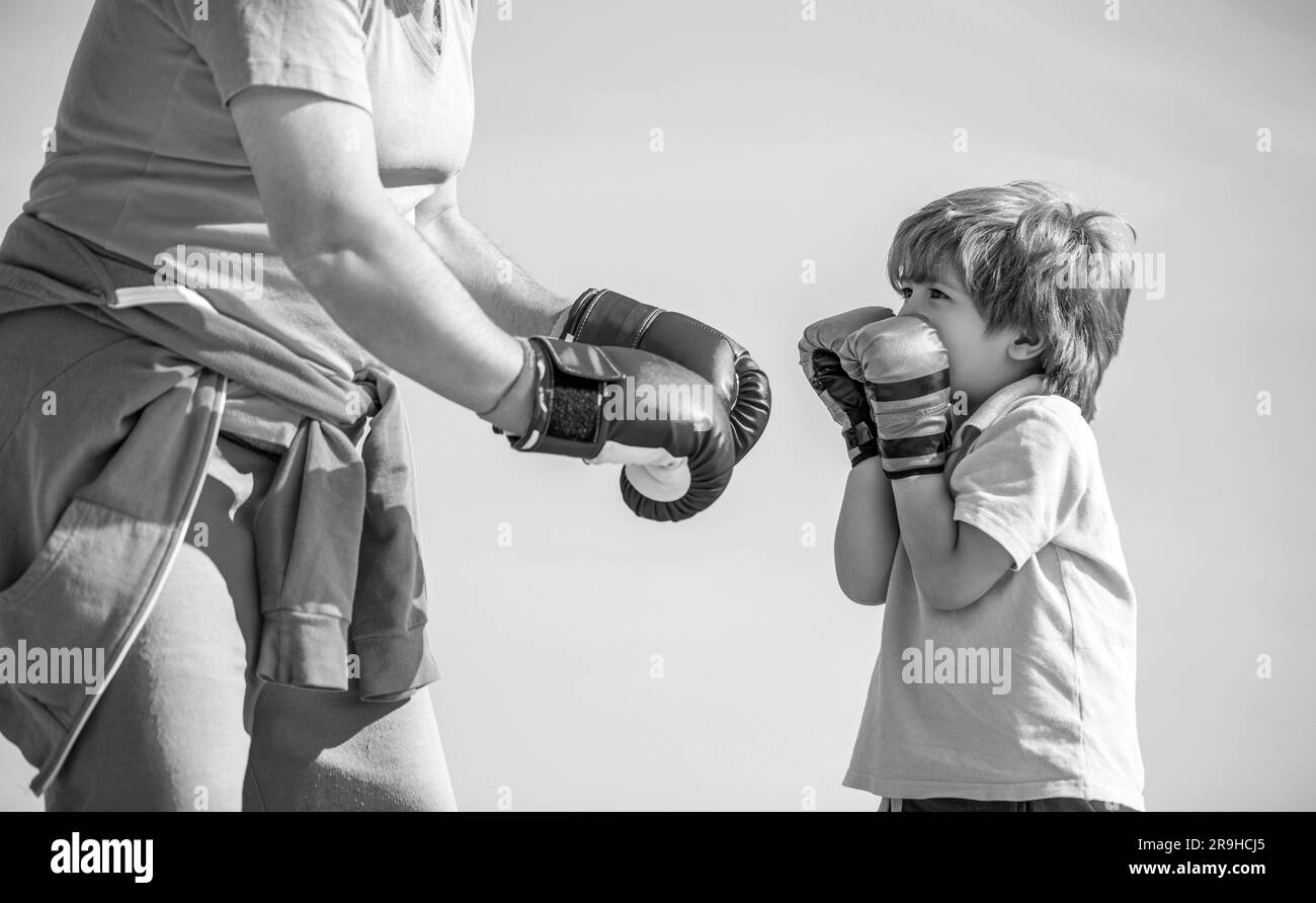 Petit sportif de garçon à l'entraînement de boxe avec entraîneur. Sportif entraîneur de boxe petit garçon dans des gants de boxe rouges. Noir et blanc Banque D'Images