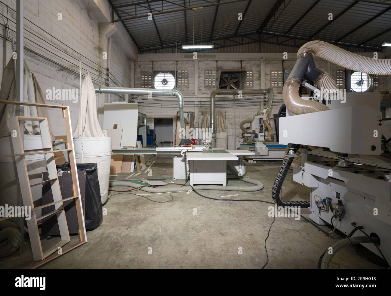 Atmosphère à l'intérieur d'une usine de meubles en bois avec des piles de contreplaqué et des machines modernes. Un ventilateur d'extraction est sur un mur de briques de béton léger dans le b Banque D'Images