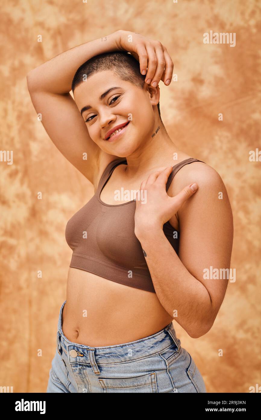 amour du corps, jeune femme curvy et heureuse en crop top posant sur fond beige marbré, regardant la caméra, représentation du corps, différentes formes, ge Banque D'Images