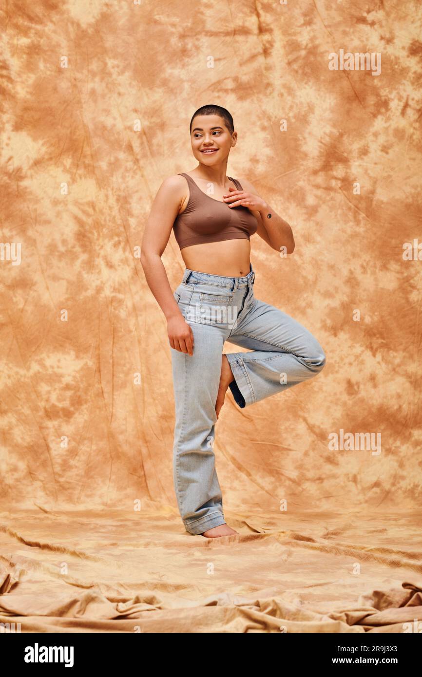 positivité corporelle, confiante, curviligne et heureuse femme en crop top et jeans posant sur fond beige marbré, tenue décontractée, auto-acceptation, génération Banque D'Images