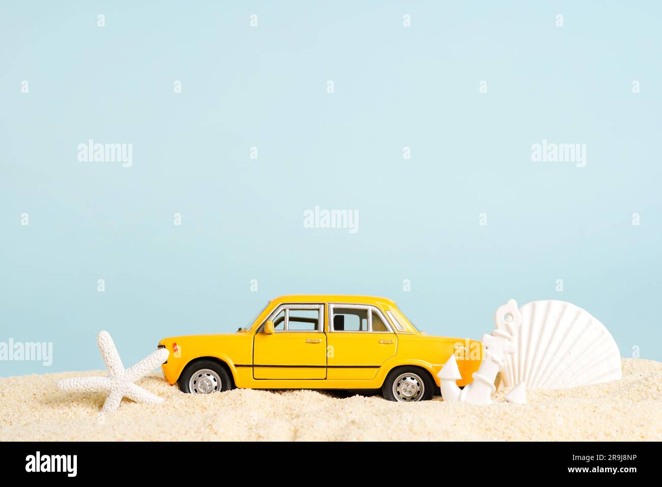 Voiture de taxi jouet avec coquillages sur le sable de plage, fond bleu. service de réservation de taxi. Déplacement. Heure d'été, espace pour le texte Banque D'Images