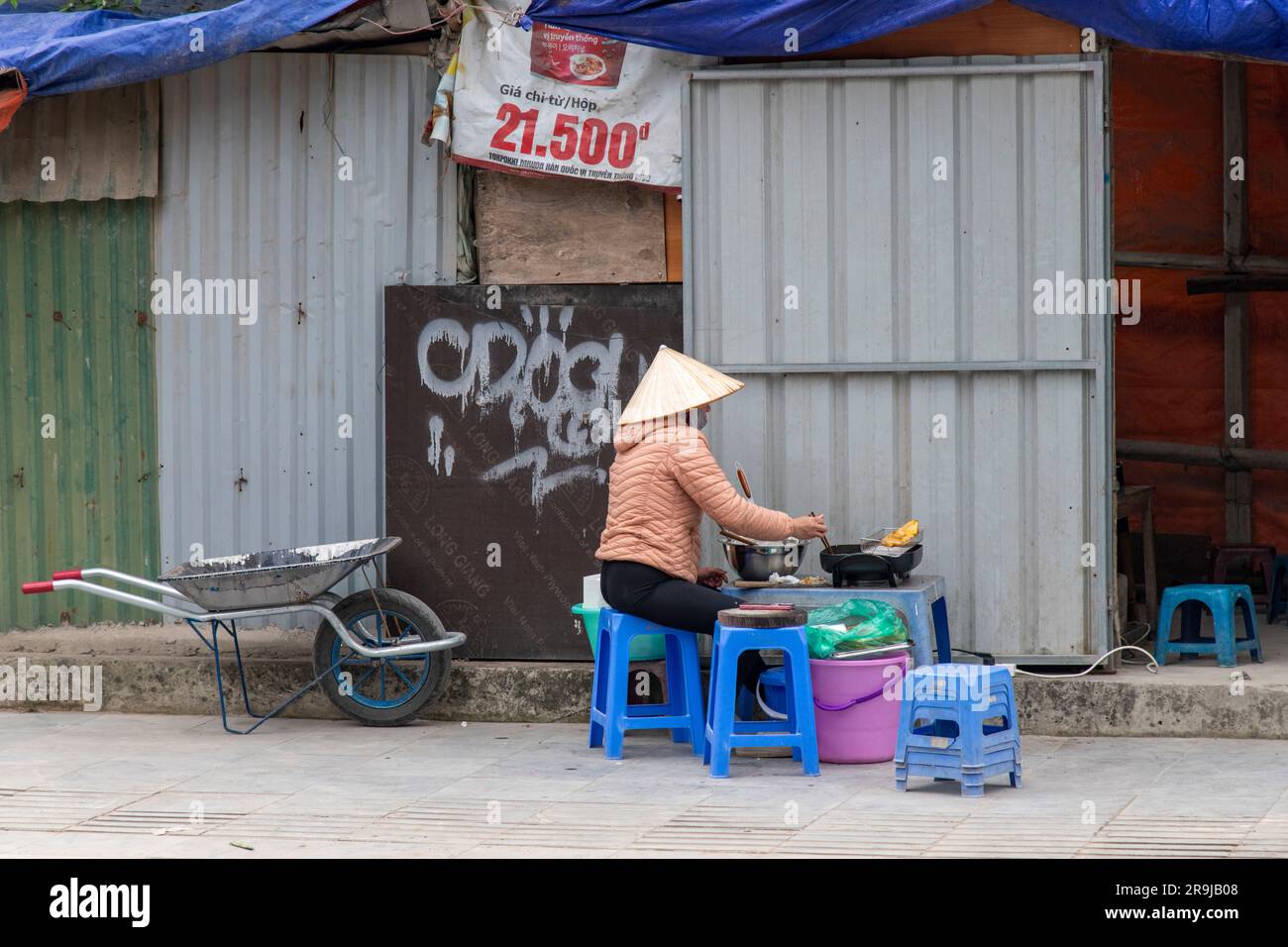 Hanoï, Vietnam-avril 2023 ; vendeur de rue assis derrière une friteuse en cours de friture dans l'un des quartiers de la ville devant un makesh Banque D'Images