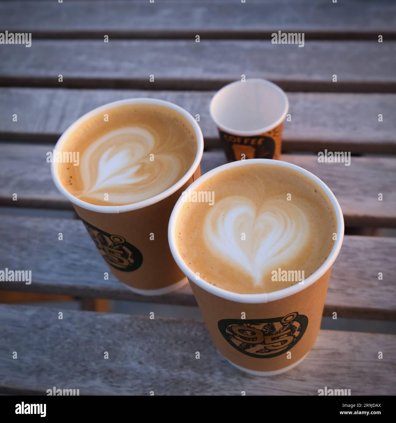 Deux tasses en papier de café avec coeur latte art sur fond de bois flou.matin café à emporter pour couple dans l'amour . Banque D'Images