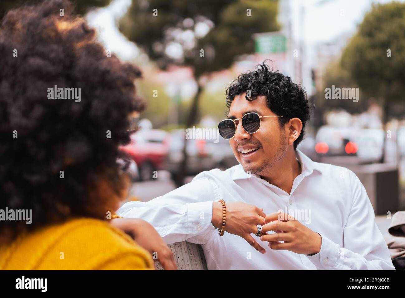 Anonyme noir femme avec cheveux afro dans des vêtements décontractés et regardant l'ami heureux de sexe masculin dans des lunettes de soleil assis sur un fond flou de la rue de ville Banque D'Images