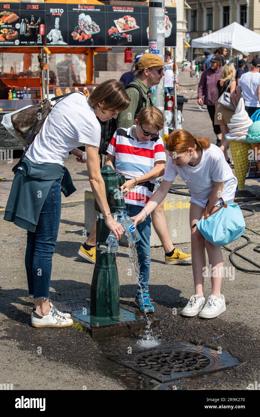 Femme et deux enfants remplissant les bouteilles d'eau douce de la fontaine lors d'une journée ensoleillée d'été sur la place du marché à Helsinki, en Finlande Banque D'Images