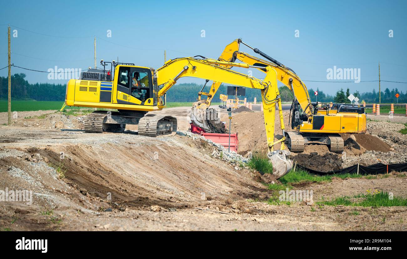 Deux pelles hydrauliques jaunes et un camion à benne basculante travaillant sur un chantier de construction de routes Banque D'Images