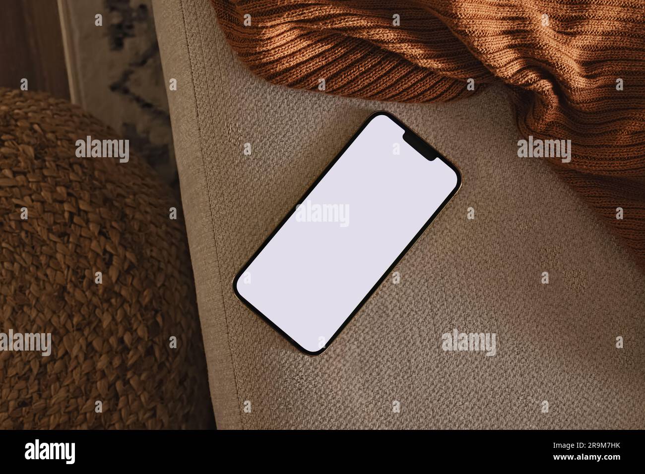 Téléphone avec écran vierge posé sur le canapé et tissu écossais brun. Design moderne et minimaliste, modèle de smartphone Banque D'Images