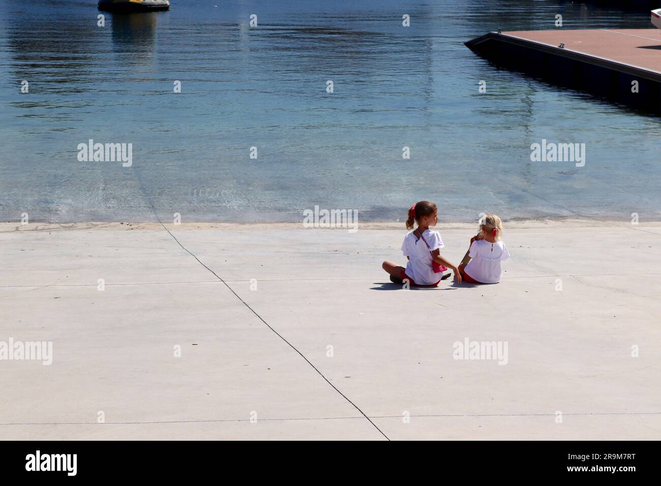 Deux jeunes sœurs vêtues de leur dimanche le mieux, profitez de la tranquillité de la mer depuis la rampe de lancement de Real Club Nautico Marina, Vigo, Espagne. Banque D'Images