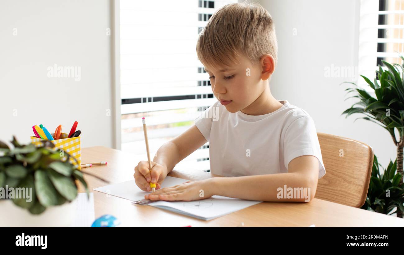 Un joli garçon fait un dessin avec une règle et un crayon. Leçons à la maison. Géométrie et dessin. Banque D'Images