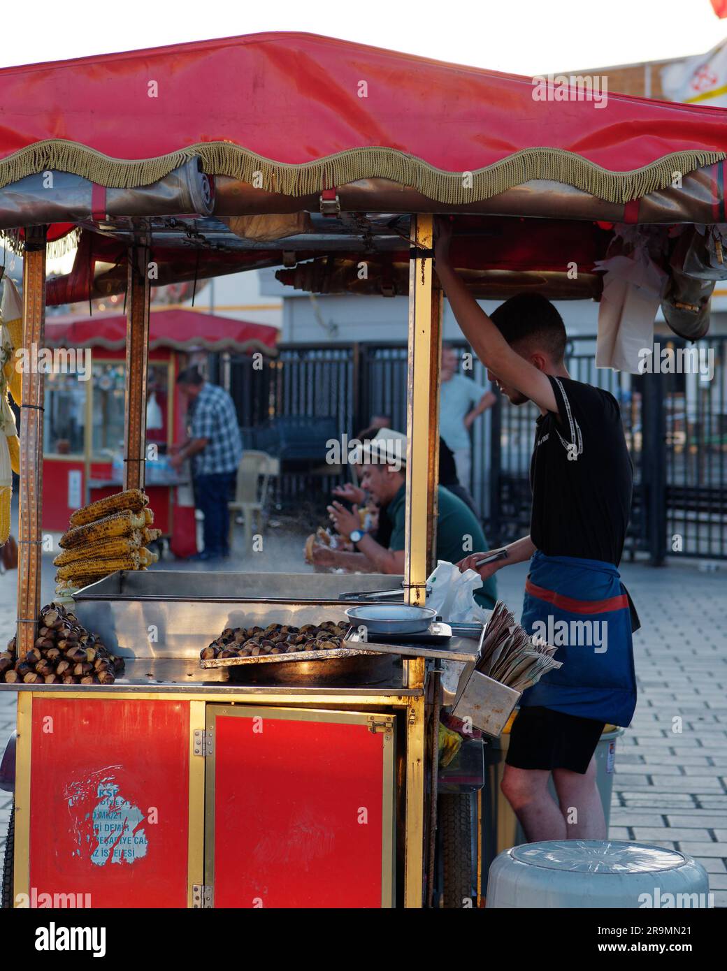 L'homme se tient à côté d'un chariot distributeur rouge un soir d'été vendant des châtaignes grillées et du maïs dans le quartier Eminonu d'Istanbul, en Turquie Banque D'Images