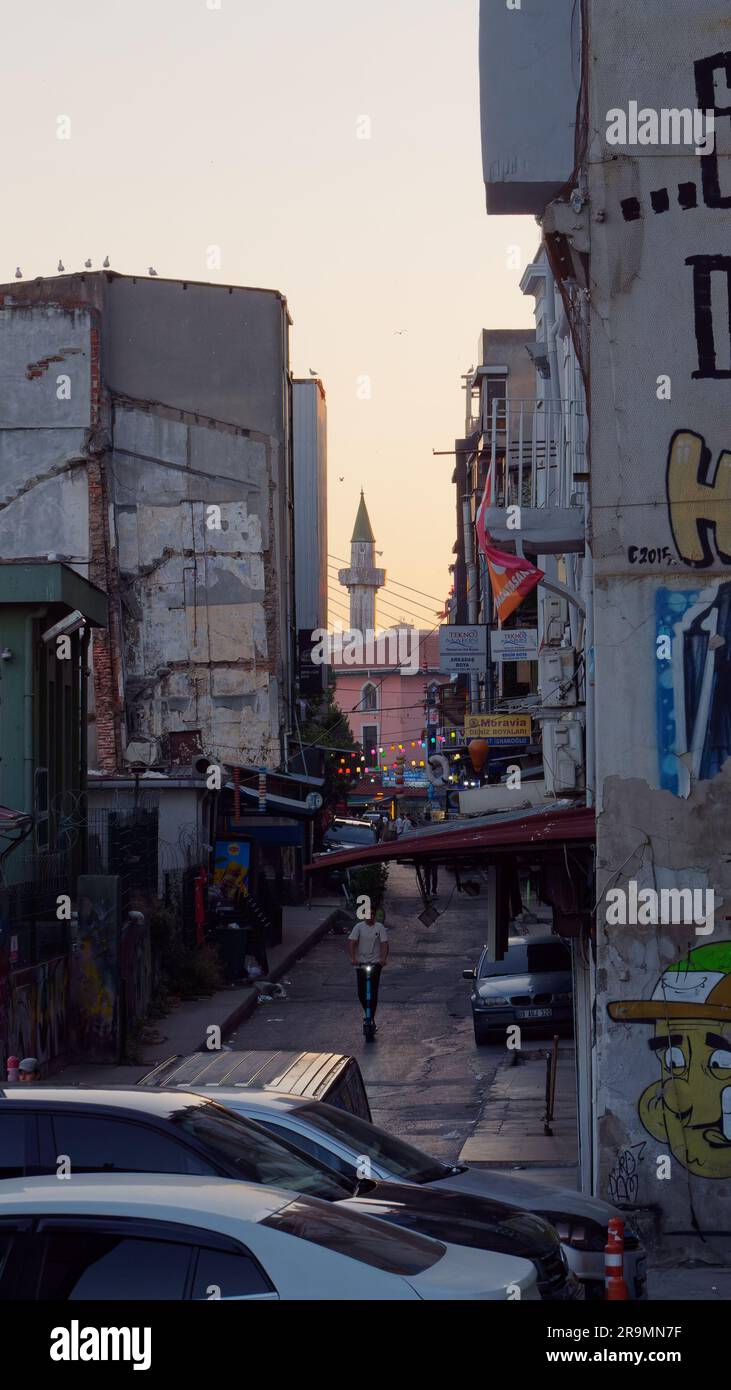 L'homme monte un scooter au milieu d'une rue étroite au coucher du soleil avec un minaret visible derrière. Istanbul, Turquie Banque D'Images