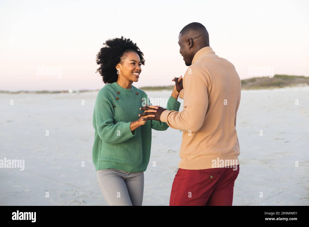 Heureux couple afro-américain dansant et souriant sur la plage au coucher du soleil Banque D'Images