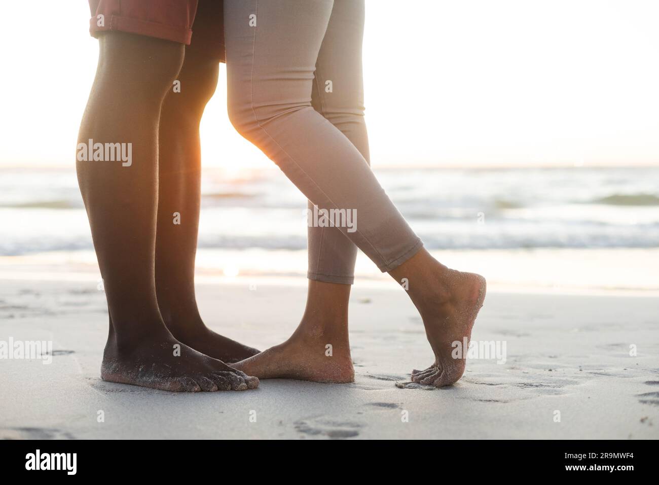 Section basse du couple afro-américain embrassant sur la plage au coucher du soleil Banque D'Images