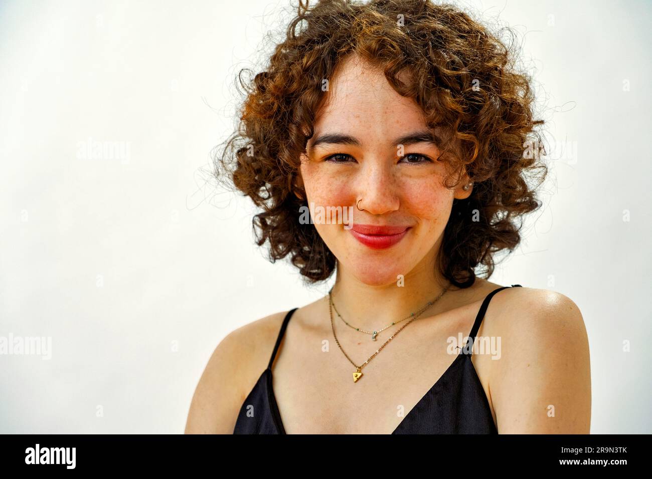 gros plan, jeune femme adulte avec des cheveux bouclés souriant, regardant l'appareil photo Banque D'Images
