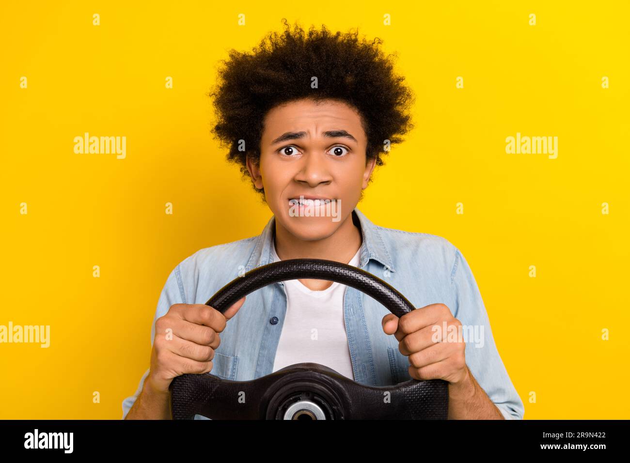 Portrait de inquiet gars port Jean veste tenir le volant mordant les lèvres se trouvent dans accident isolé sur fond jaune Banque D'Images