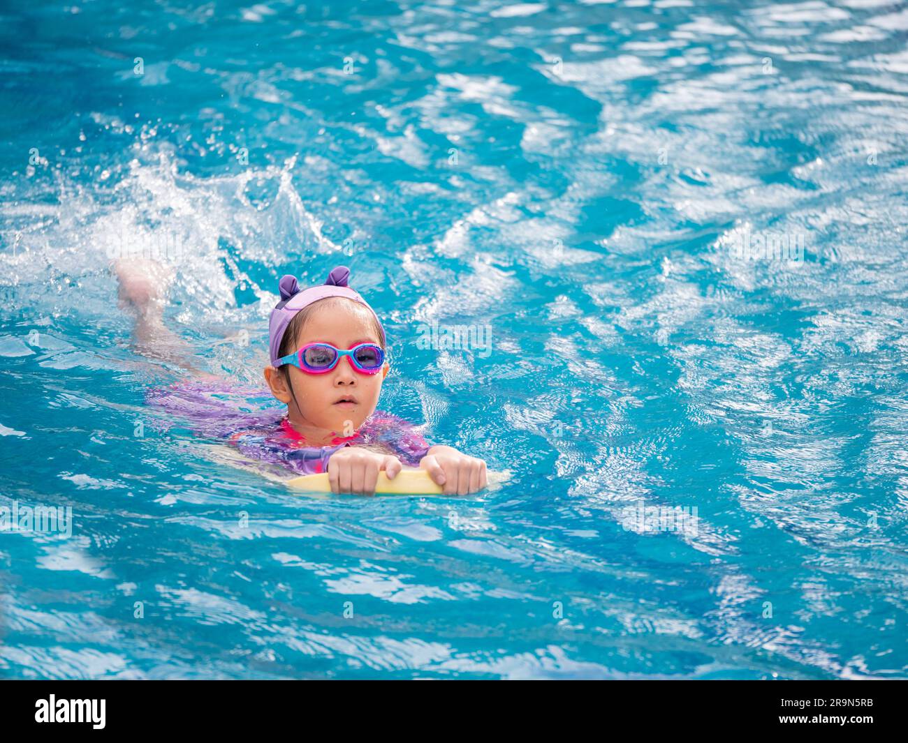 Enfant asiatique ou petite fille portant un maillot de bain pour apprendre à la piscine, apprendre et s'entraîner à nager sur le kick board Banque D'Images