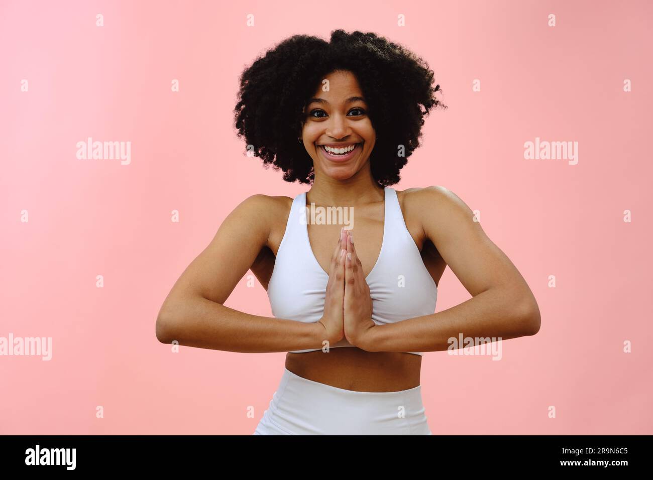 Portrait d'une jeune femme noire portant des vêtements de sport faisant du yoga, en position de prière, sur fond de studio rose Banque D'Images