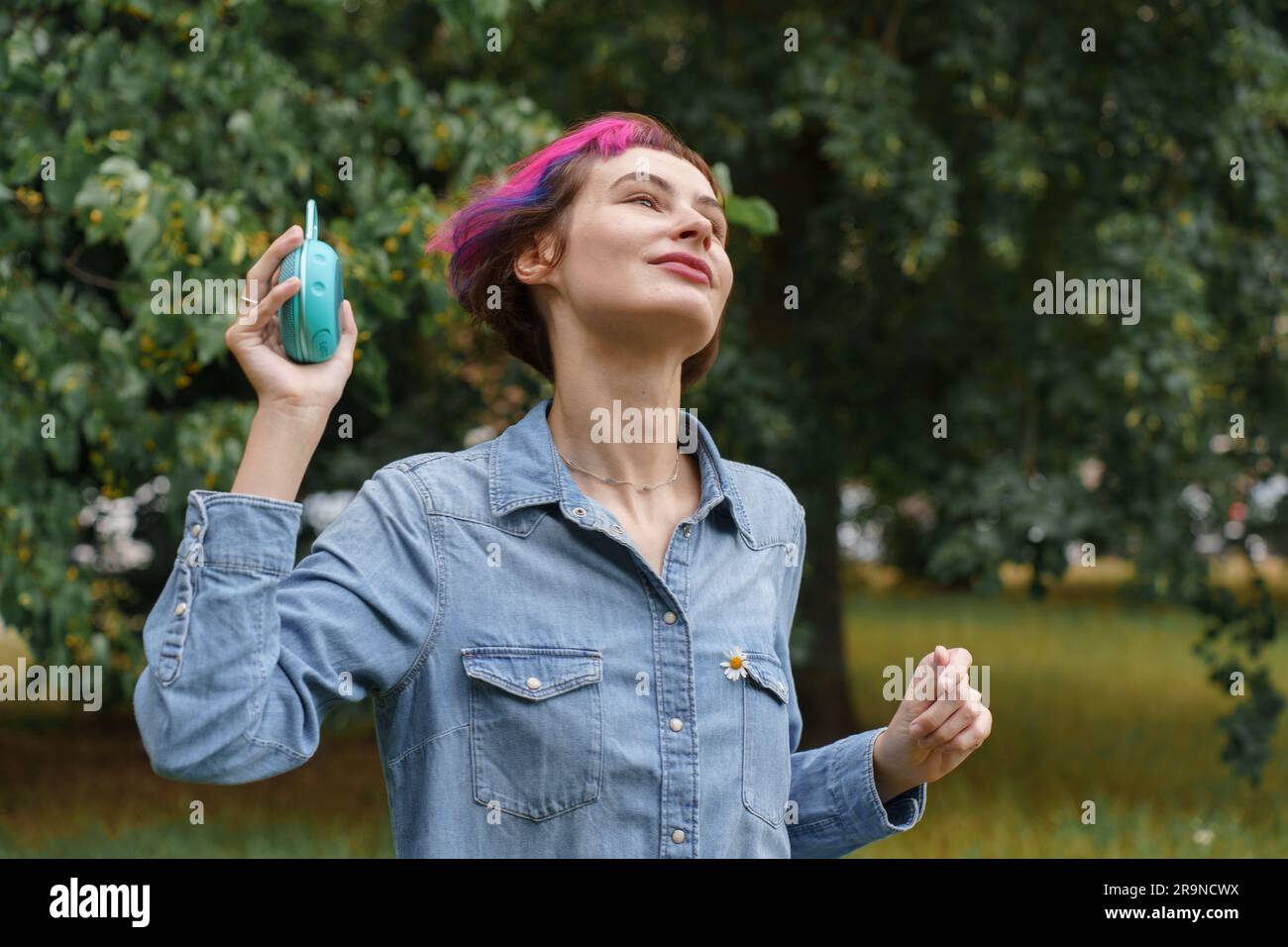 Une femme aux cheveux roses écoute de la musique à travers le haut-parleur musical portable dans le parc Banque D'Images