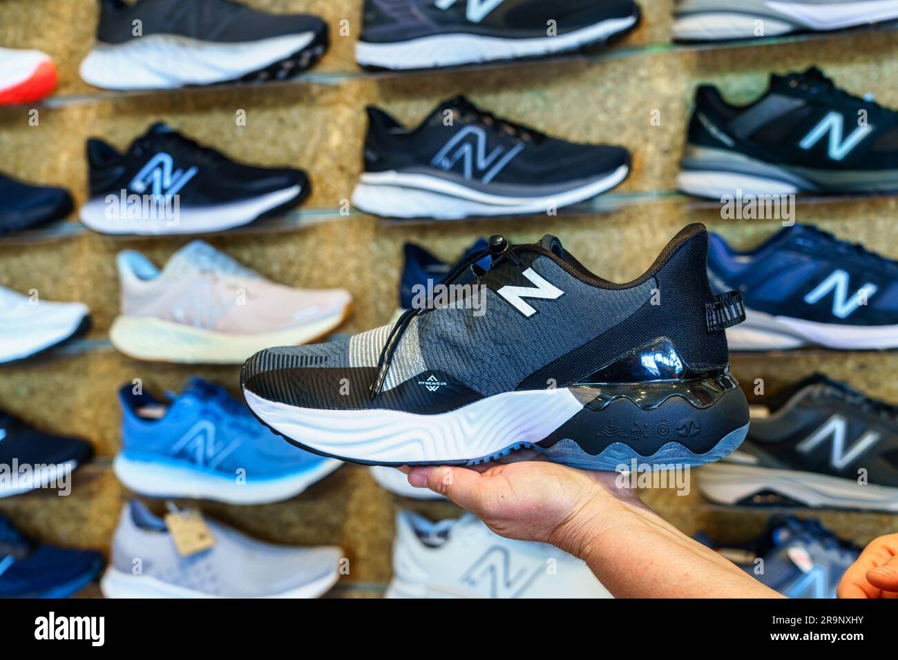 Main d'une cabas féminine tenant une chaussure New Balance Banque D'Images