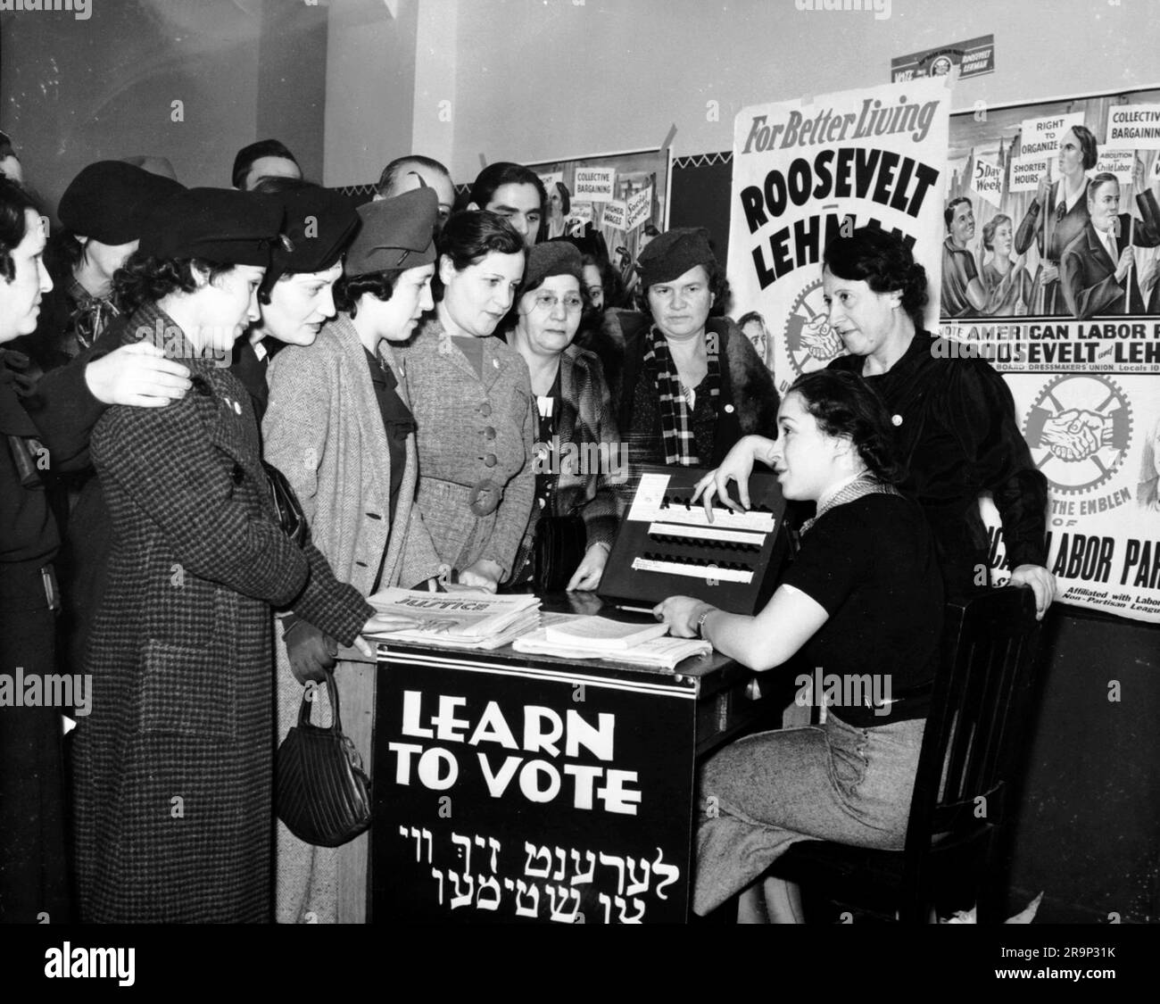 Des femmes entourées d'affiches en anglais et de yiddish soutenant Franklin D. Roosevelt, Herbert H. Lehman et le Parti travailliste américain enseignent à d'autres femmes comment voter, 1935. Banque D'Images