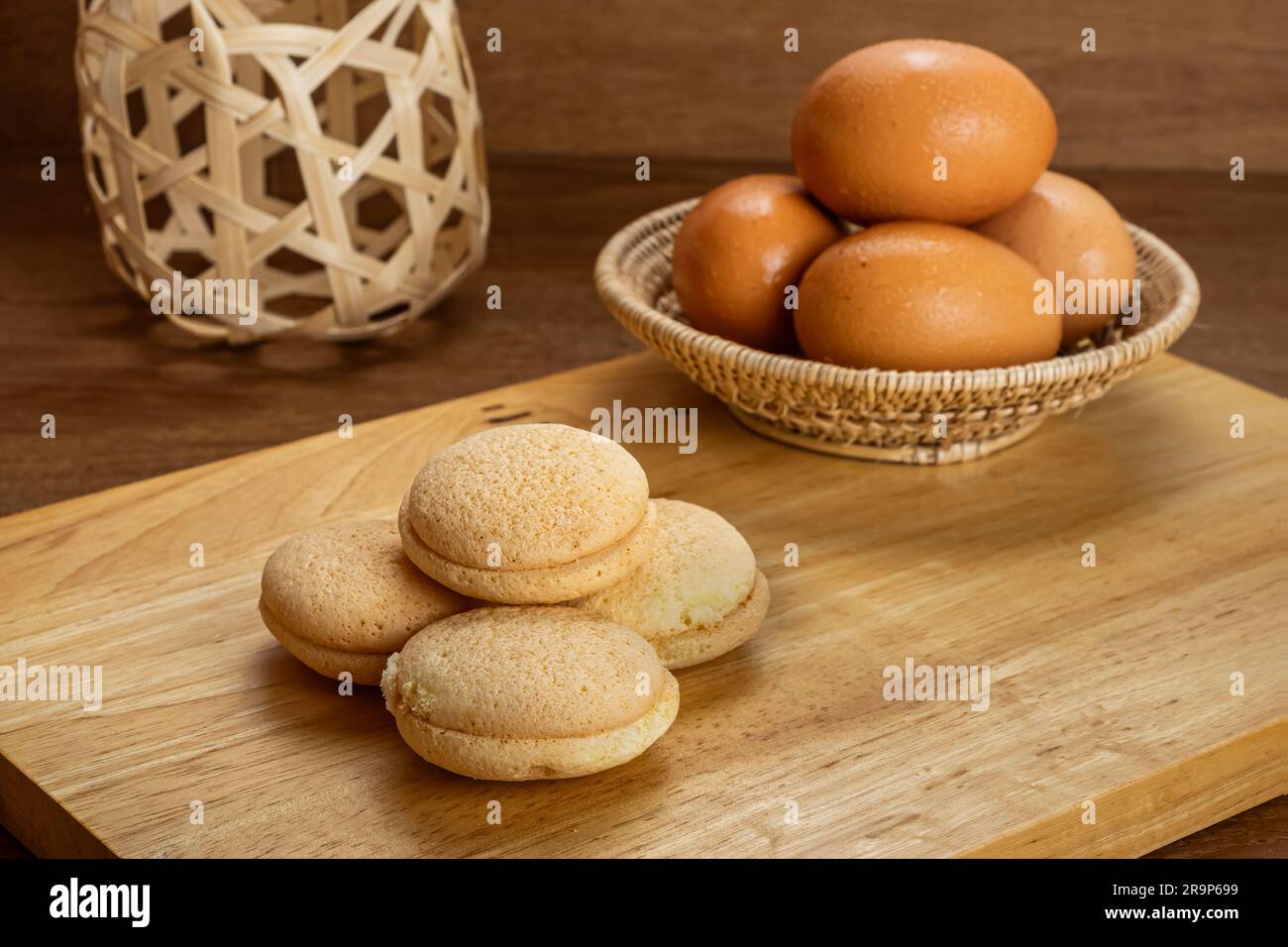 Vue à grand angle pile de petit gâteau sucré maison rempli de confiture d'ananas sur une planche en bois avec pile d'oeufs de poulet dans un panier en bambou sur une table en bois Banque D'Images